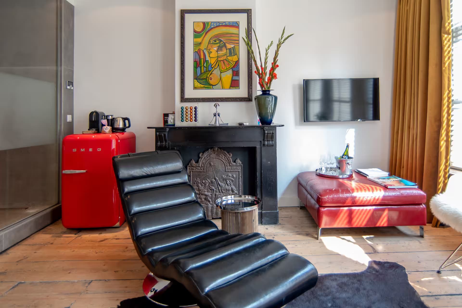 Double Fun — zithoek met zwarte chaise longue, rode Smeg mini-koelkast en oude haard met kunstwerk