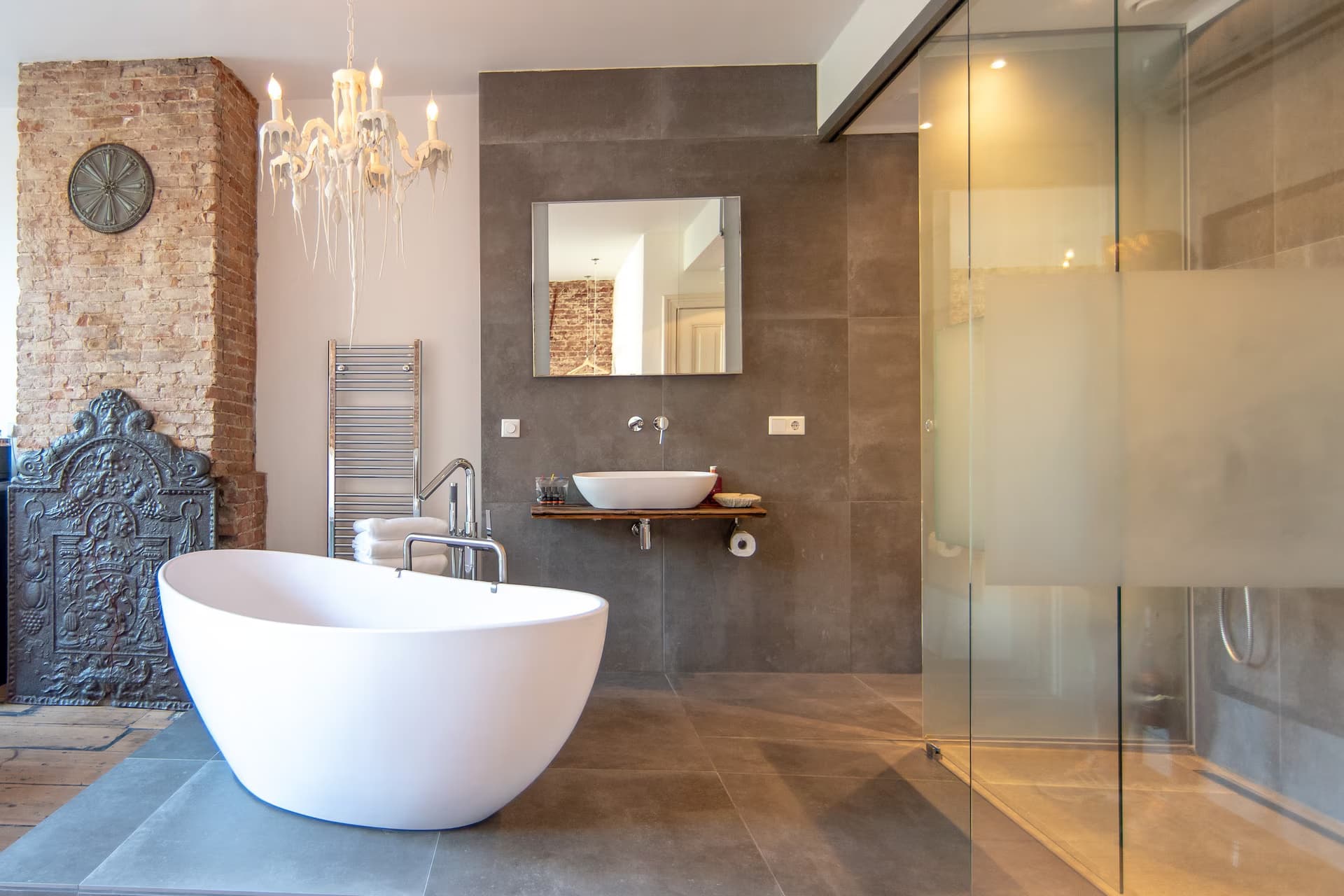 Love Suite — open badkamer met vrijstaand bad in marmer, kroonluchter en regendouche achter glas